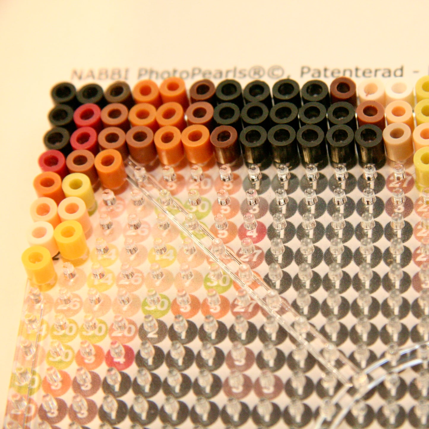 Närbild på en transparent piggplatta med färgade plastpärlor placerade enligt ett PhotoPearls mönster med färgsystem.
